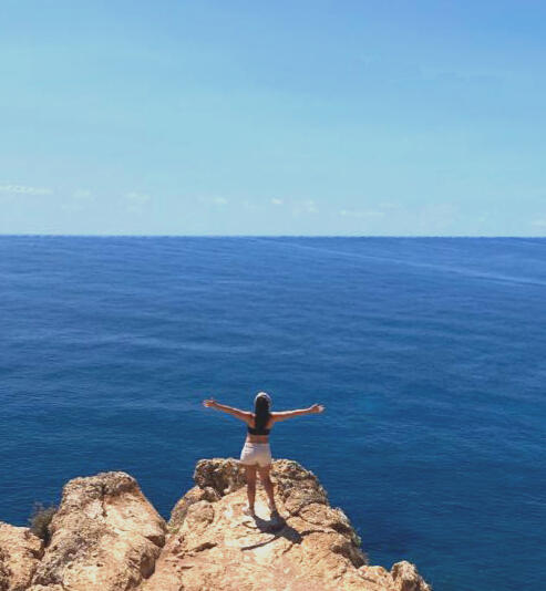 Flor de espaldas con los brazos abiertos frente al mar, simbolizando apertura, libertad y conexión interior en una sesión de Reg Apertura y libertad en tu proceso